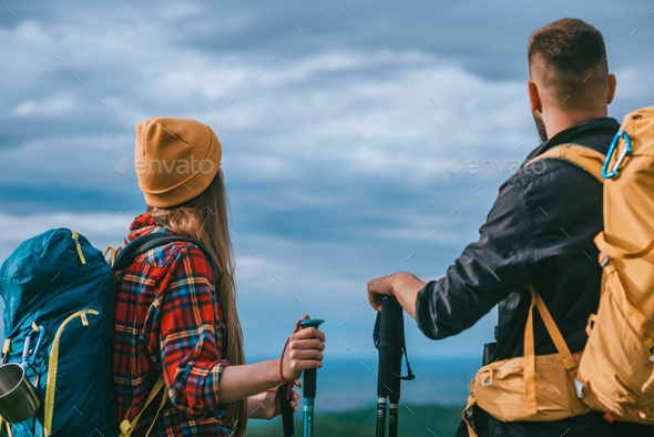 Couple of hikers using trekking poles and wearing backpacks with a ...