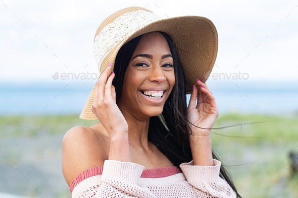 Pretty African American woman with black hair wearing a floppy hat at the ocean beach