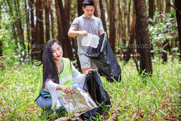 Two volunteers, Asian male and female, are helping to pick up waste by black garbage bags in park