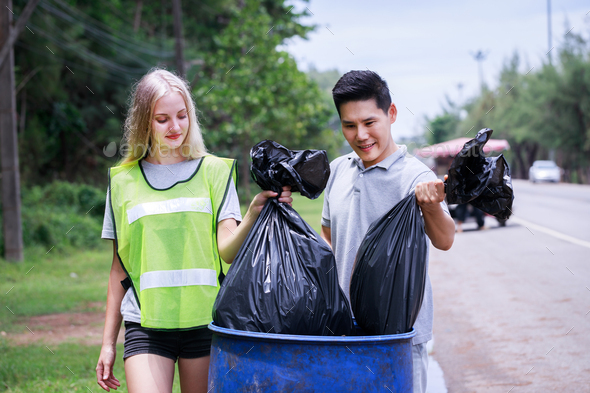 Two volunteers, Asian males and Caucasians are helping to pick up waste by garbage bags beside road