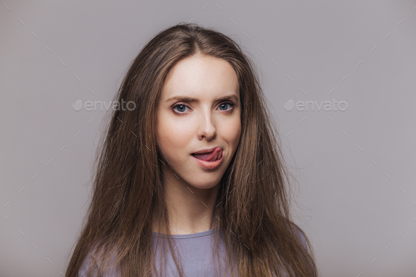 Female licks lips with tongue, dressed casually, isolated over grey ...