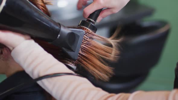 Female hairdresser blow drying hair of female customer at hair salon alt