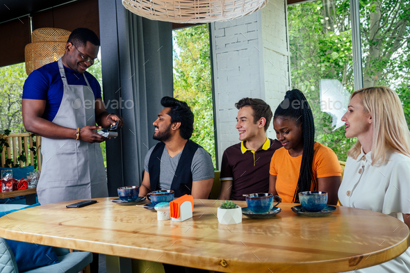 mixed-race friends paying to waiter payment machine in cafe