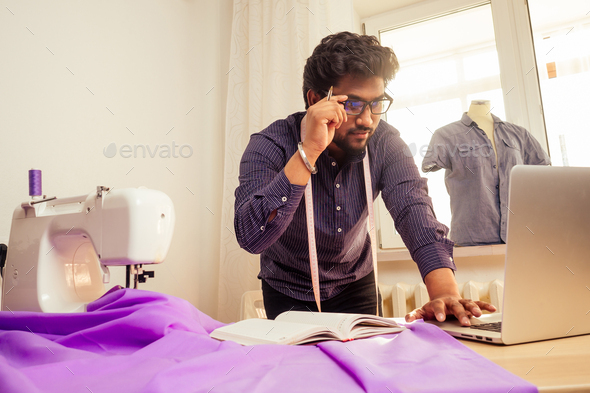 handsome indian tailor man In a stylish shirt workinh with violet cotton textile