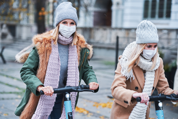 Girl friends wearing face masks and commuting on scooter in the city