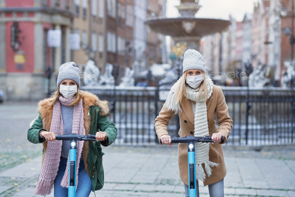 Girl friends wearing face masks and commuting on scooter in the city
