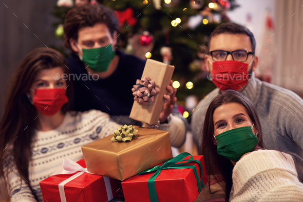 Group of friends wearing masks exchanging Christmas presents at home
