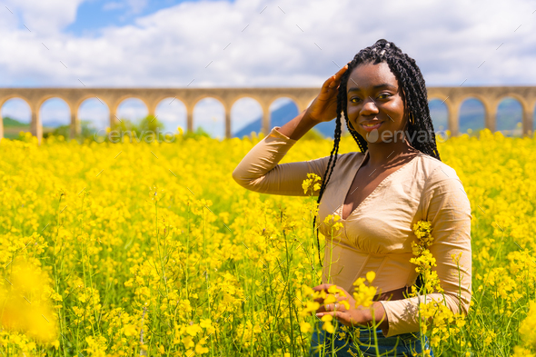 Portrait of a black ethnic girl with braids looking at camera, trap music dancer, yellow flowers