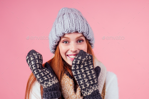 redhaired ginger woman wearing stylish hat ,knitted mittens and sweater in studio pink background