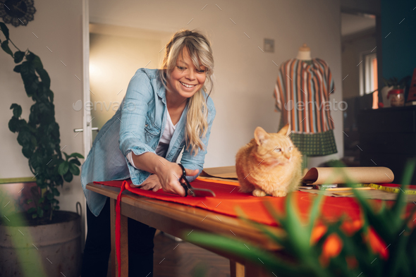 Woman tailor working from home and tailoring beautiful clothes with a pet cat