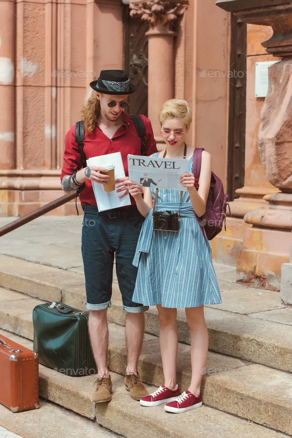 couple of tourists with coffee reading travel newspaper while standing on stairs with retro