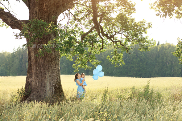 Woman with a child with balloons under a big oak tree with mighty branches
