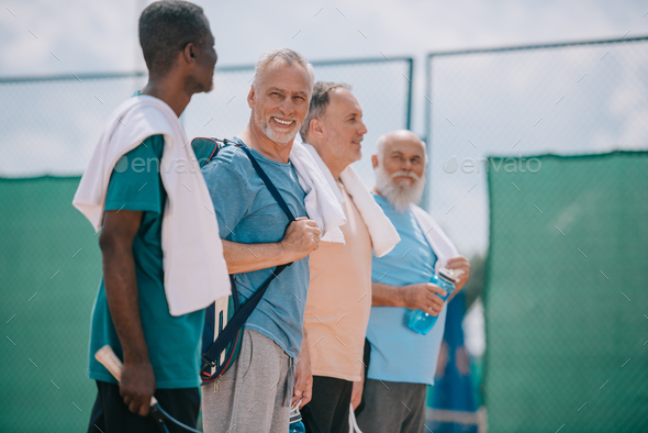 side view of multicultural elderly men with towels and tennis equipment on tennis court