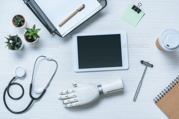top view of doctor workplace with prosthetic arm, stethoscope, reflex hammer and digital tablet with