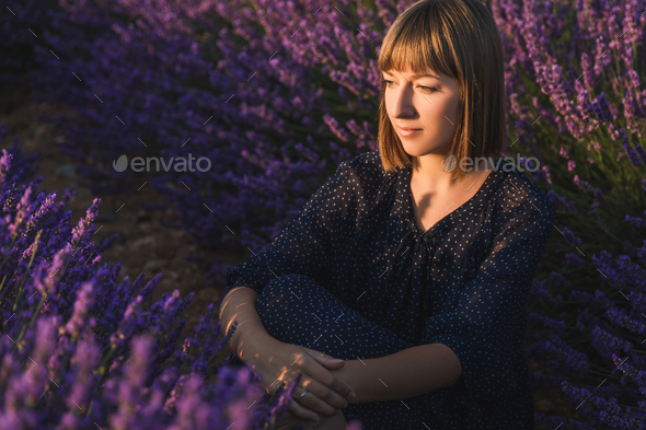 beautiful pensive girl sitting at lavender field and looking away, provence, france