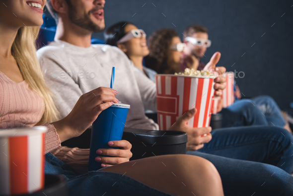 partial view of emotinal multiethnic friends with popcorn watching film together in movie theater