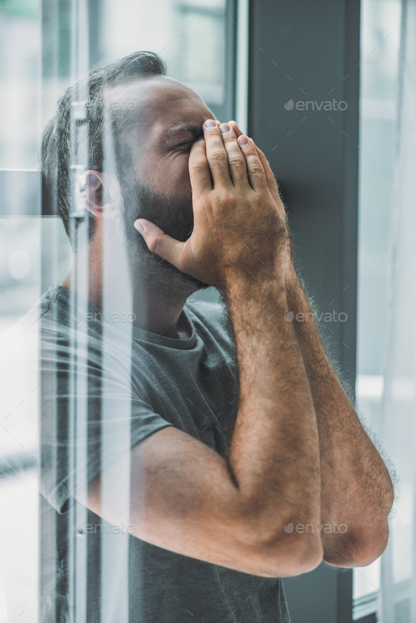 side view of depressed frustrated bearded man crying with hands on face