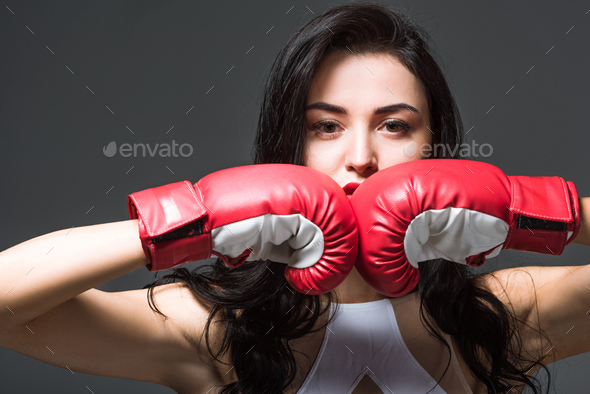 woman in boxing gloves looking at camera isolated on grey