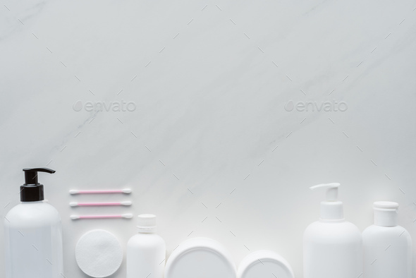top view of bottles of cream, cosmetic pads and cotton swabs on white surface, beauty concept