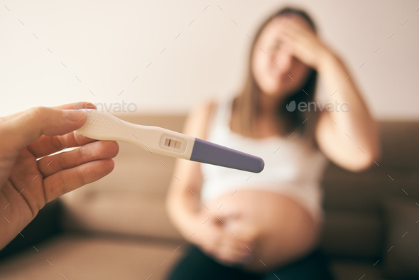 Selective focus of pregnancy test and sad lady at background