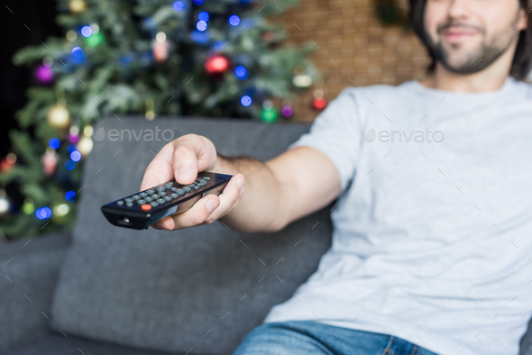 close-up view of man using remote controller while sitting on couch at christmas time