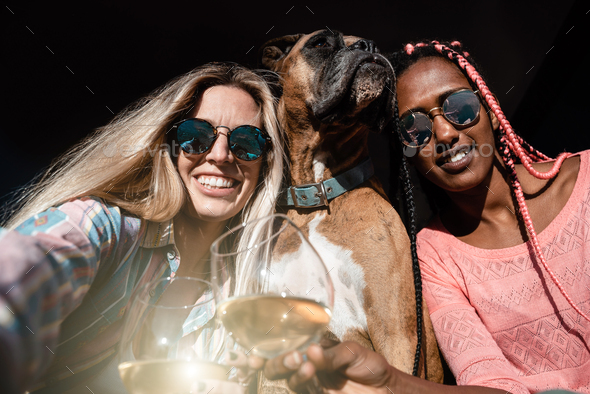 Young multiracial friends and pet dog celebrate with wine while doing a selfie - Focus on right girl
