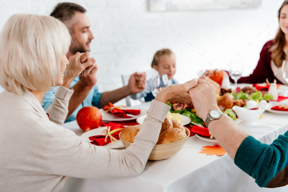 family holding hands and praying together before thanksgiving dinner at served table with turkey