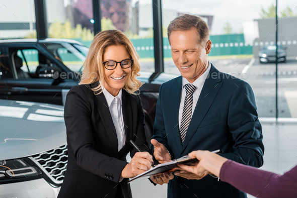 happy business couple signing papers for buying new car in showroom