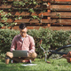 focused asian freelancer working on laptop on green grass with coffee to go and notebook in park - PhotoDune Item for Sale