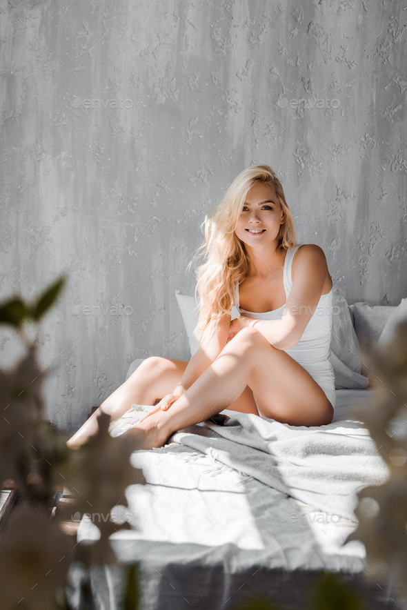 selective focus of attractive blonde girl in underwear sitting on bed and  smiling at camera Stock Photo by LightFieldStudios