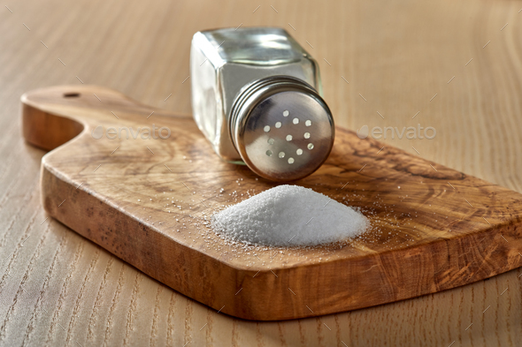 Spilled salt and a salt shaker on a cutting board