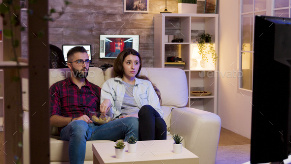 Couple sitting on couch and eating chips while watching a movie