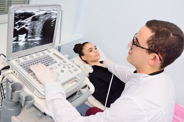 doctor performs an ultrasound examination of the thyroid gland of a young, pretty woman in a modern