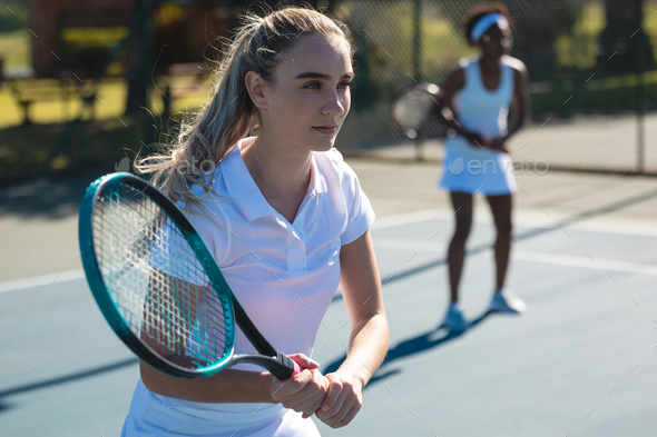 Beautiful young female caucasian female player with african american partner at tennis court