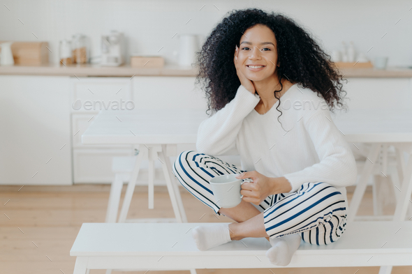 American woman wears white jumper, striped pants, socks, poses on with Stock Photo by