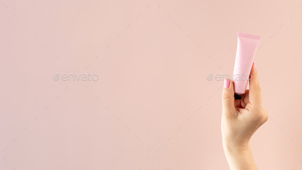 Mockup of a pink tube with a cosmetic product in a female hand on a light pink background.