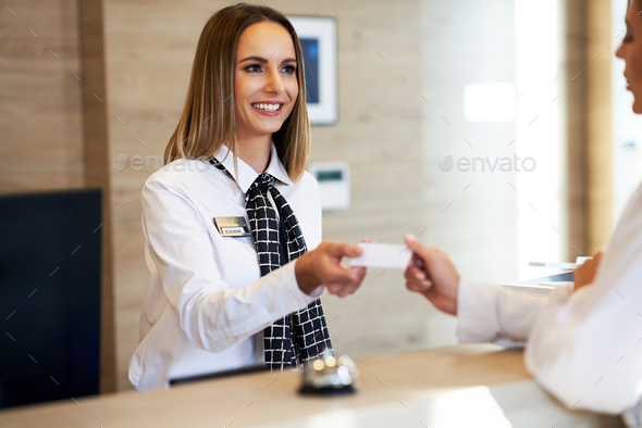 Receptionist giving key card to businesswoman at hotel front desk