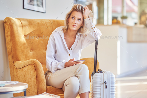 Businesswoman with luggage in modern hotel lobby using smartphone