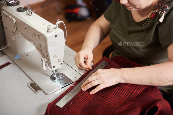 Woman preparing textile for sewing: measuring plaid textile with ruler, fixing edges of fabric