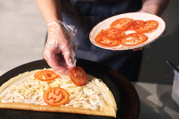 Chef keeping plate with cutted tomato. Woman hand putting tomato slices on pancake lubricated