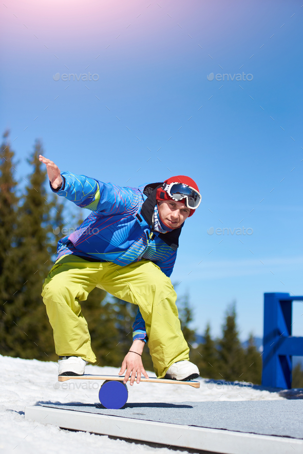 Snowboarder keeps balance on the trainer board with roller at mountains.