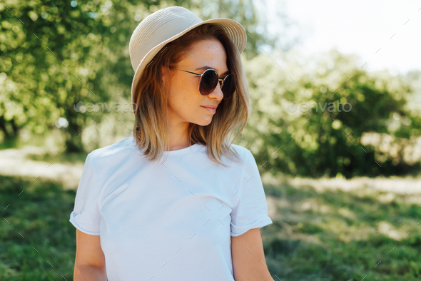 Close-up portrait of pretty young woman wearing round glasses, straw hat  and white t-shirt outdoors Stock Photo by SergioPhotone