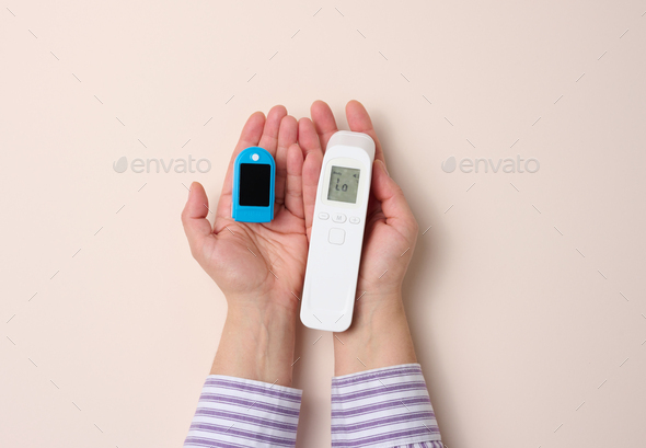 Female hand holds plastic non-contact thermometer and oximeter on beige background