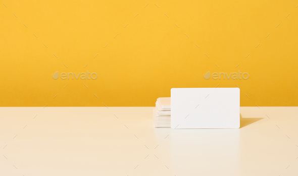 Stack of white rectangular business cards on a yellow background, company branding, address.