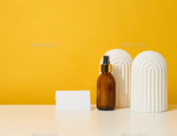 Glass brown bottle with cosmetic spray on a yellow background