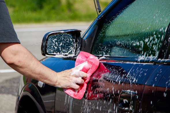 Man is washing car outside. Hand cleaning car. Male hand holding pink sponge with foam