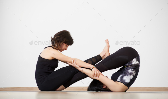 People practicing yoga lesson with female partner performing Plow and Seated Forward Fold pose