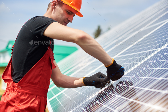 Electrician in black t-shirt and gloves is installing solar cell to save energy against blue sky