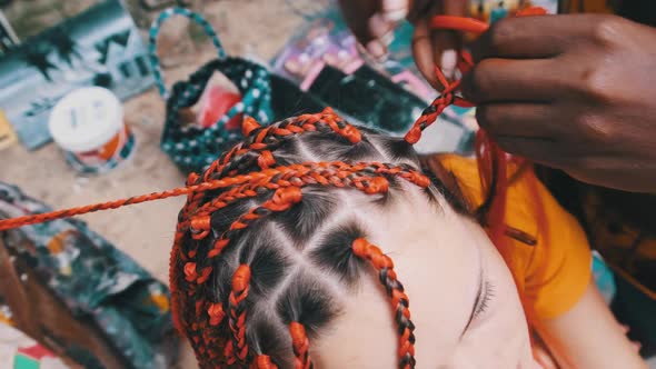 Process of Weaving African Braids with Red Kanekalon Outdoor Zanzibar Africa alt