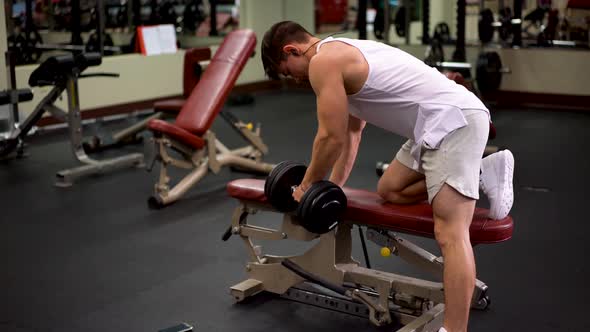Rear side shot of young bodybuilder doing one arm dumbbell rows using a bench. alt